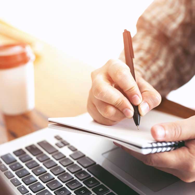 person taking notes next to a computer